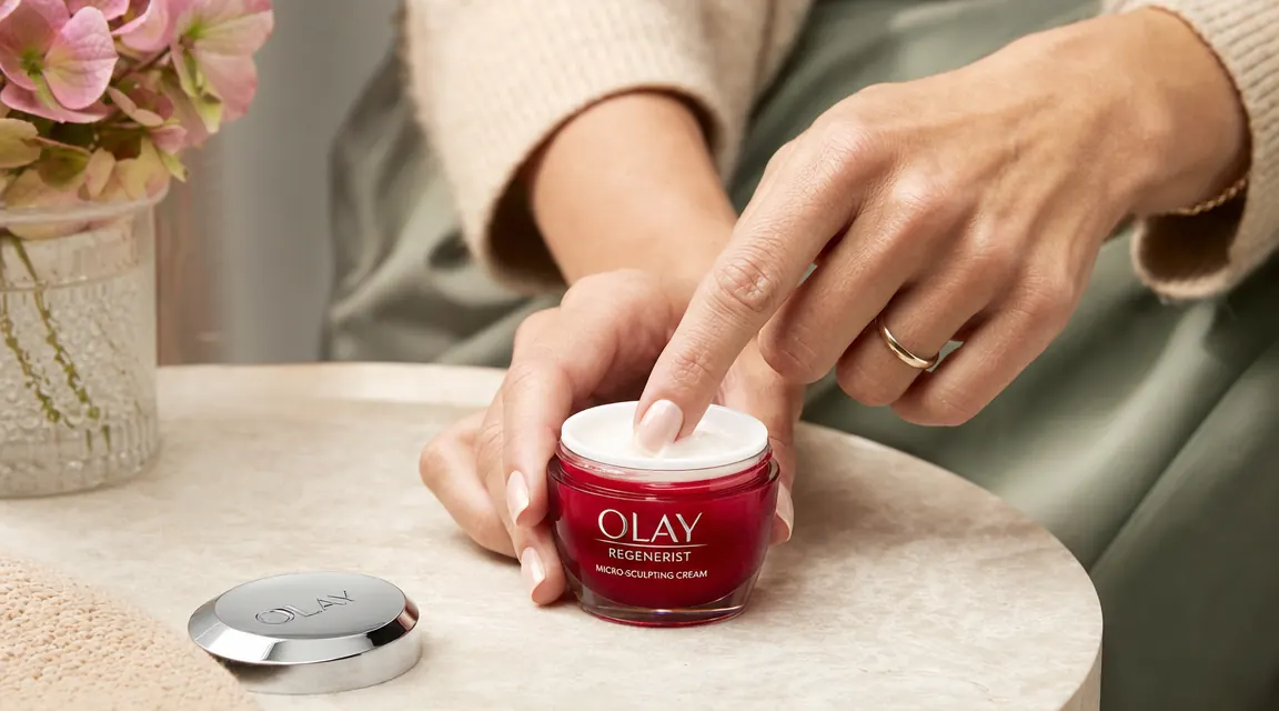 Hand scooping a small amount of Olay Regenerist cream from the jar with one finger, cream visible in natural light
